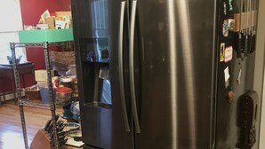 A stainless steel Samsung refrigerator with a water dispenser, located in a kitchen with tiled flooring and a wooden table in the background. - Classy AF Home Steps from Colby and Trails (Oakland)