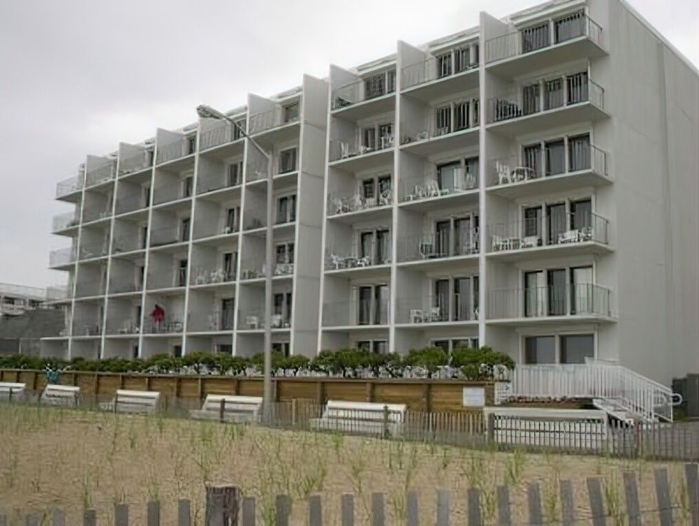 A multi-story building with balconies, a wooden fence, and a grassy area in front.