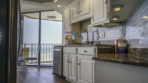 A kitchen with white cabinets, a granite countertop, and a view of the ocean through a sliding glass door. - Premium-Steps 2 Beach-Wide Oceanview-Lrg Balconies-Pool-Gated-On Site Restaurant (Myrtle Beach)
