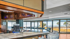 A modern bar area with a coffee machine, seating, and large windows overlooking the beach. - Premium-Steps 2 Beach-Wide Oceanview-Lrg Balconies-Pool-Gated-On Site Restaurant (Myrtle Beach)