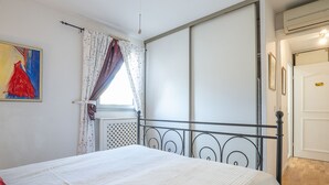 Un dormitorio con cama, ventana con cortinas, radiador y puerta.