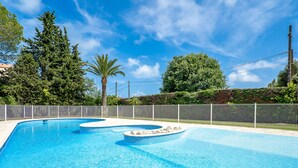 Una piscina azul cristalina con dos jacuzzis, rodeada por una cerca y árboles.