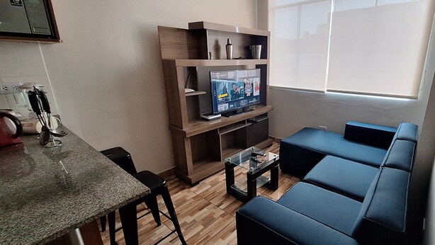 Un espace de vie compact comprenant un canapé, une table basse, un téléviseur posé sur un meuble en bois et un coin repas avec des chaises.