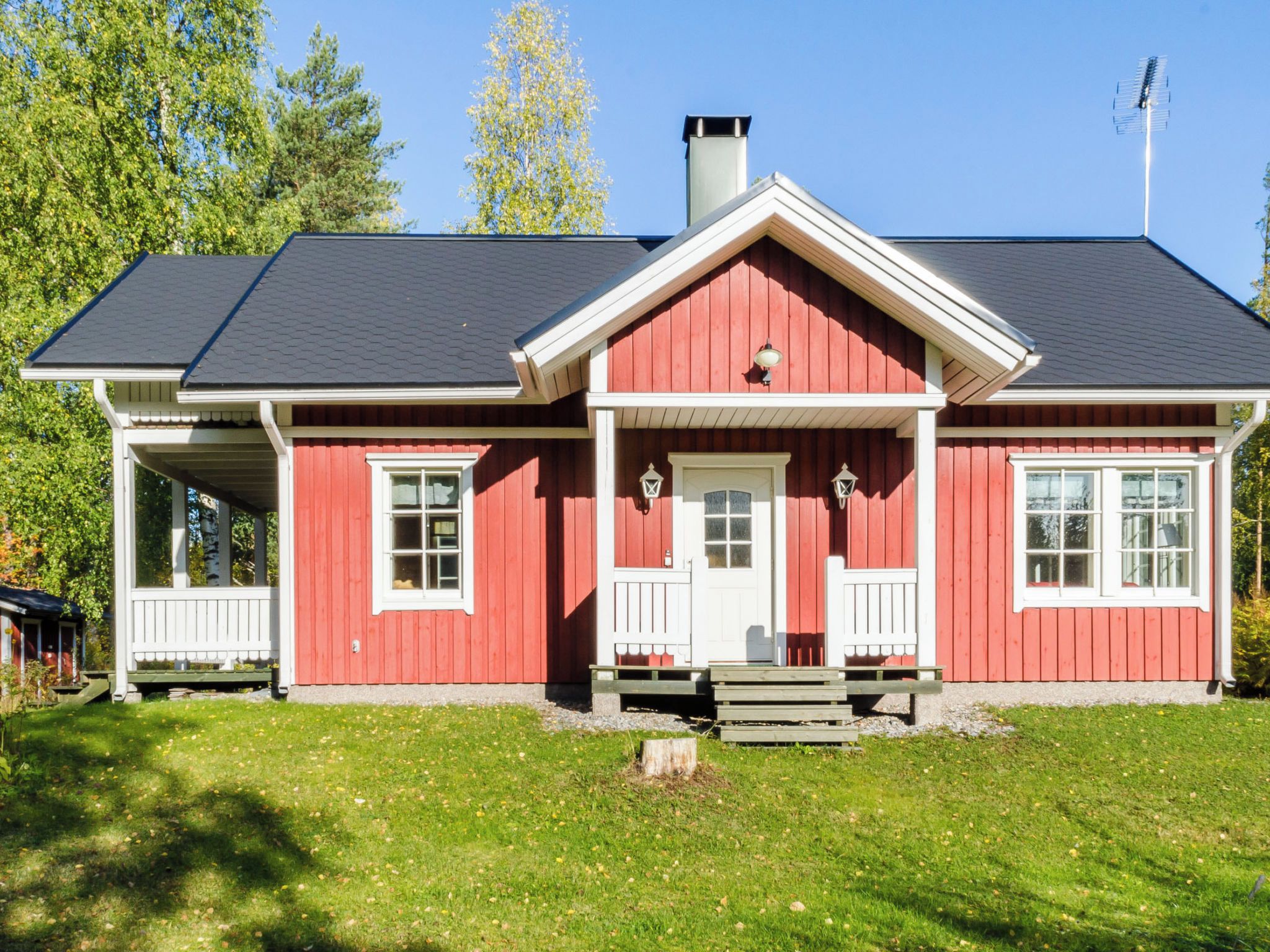 Ett rött hus med en vit veranda, en skorsten och en klarblå himmel.