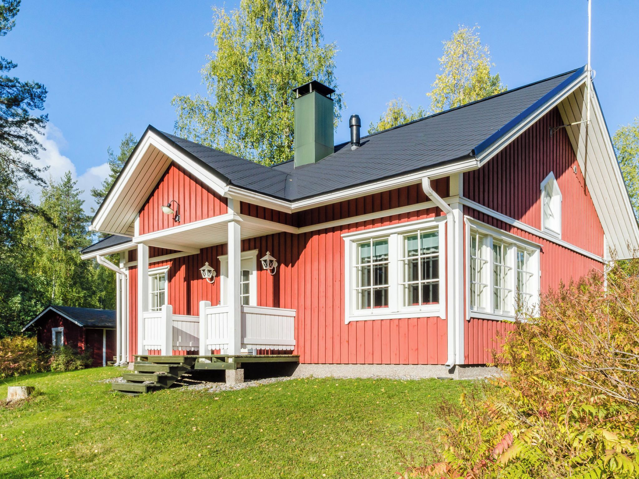 Ein rotes Holzhaus mit Veranda, weißem Zierdekor und Schornstein.