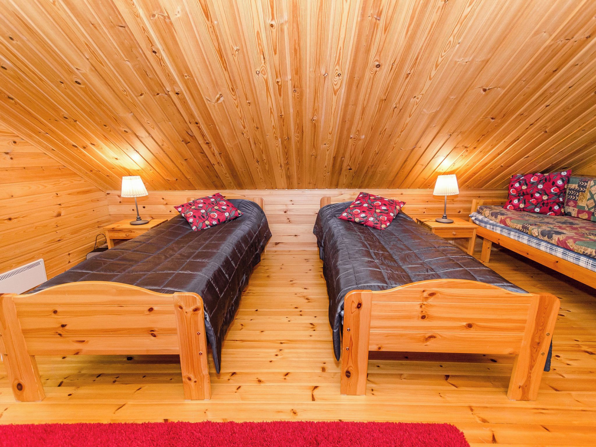 Een knus zolderkamer met twee houten bedden, een rood tapijt en een bank met gestreepte kussens.