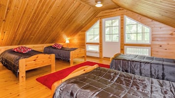 A cozy attic bedroom with wooden walls and sloped ceilings, featuring two beds with red and black bedding and a red rug.