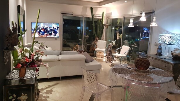 En moderne stue med en hvid sofa, et glasbord og et fjernsyn, der viser en sportsbegivenhed.