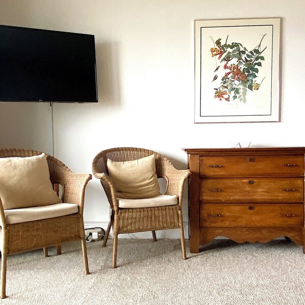 A living room with two wicker chairs, a wooden dresser, and a framed botanical print on the wall. - Edgewater House - Ocean Front Units With Spectacular Views! (Rehoboth Beach)