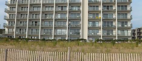 A multi-story hotel with balconies, a sandy foreground, and a clear sky.