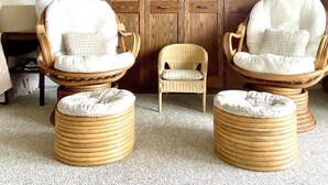 Una habitación con dos sillones de mimbre y otomanas, una pequeña silla de madera y un amplio armario de madera.
