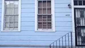 A two-story building with a light blue exterior, numbered 1425, featuring a black metal gate and a small balcony with a metal railing. - Historic Lower Garden District 1BR • Near St. Charles Streetcar (New Orleans)
