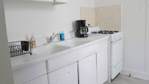A kitchen with white cabinets, a stove, a sink, and a coffee maker. - Historic Lower Garden District 1BR • Near St. Charles Streetcar (New Orleans)