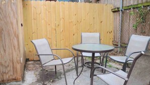 A patio with a round table and four chairs, a wooden fence, and a chain-link fence in the background. - Historic Lower Garden District 1BR • Near St. Charles Streetcar (New Orleans)