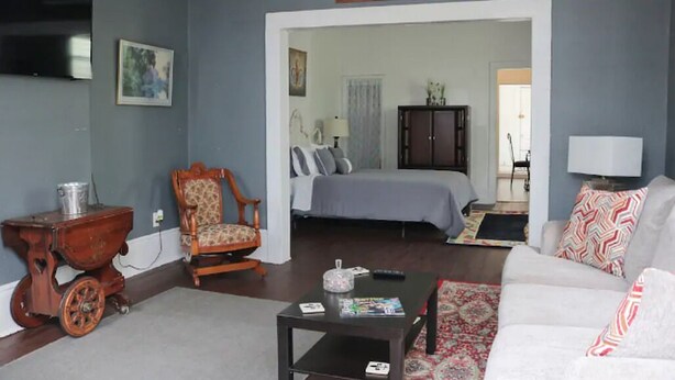 A living room with a sofa, a coffee table, a rocking chair, and a television. - Historic Lower Garden District 1BR • Near St. Charles Streetcar (New Orleans)
