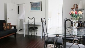 A dining area with a glass table and metal chairs, a white door, and a framed picture on the wall. - Historic Lower Garden District 1BR • Near St. Charles Streetcar (New Orleans)