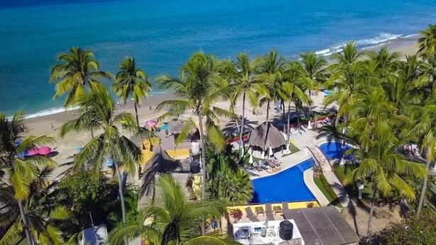 A beach resort with a pool, palm trees, and a view of the ocean.