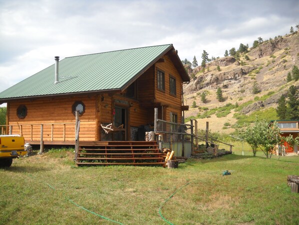 A log cabin with a green metal roof, a porch with a bench, and a small deck. - Trout Tales Lodge, Dearborn River front, blue ribbon fishing. Cascade, Craig MT. (Cascade)