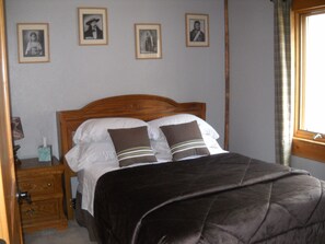 A bedroom with a wooden bed, two pillows, a bedside table with a lamp, and framed pictures on the wall. - Trout Tales Lodge, Dearborn River front, blue ribbon fishing. Cascade, Craig MT. (Cascade)