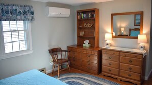 Ein Schlafzimmer mit einem Bett, einem hölzernen Schminktisch, einem Sessel, einem Bücherregal, einem Spiegel und zwei Nachttischlampen.