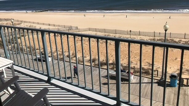 Vista a la playa desde un balcón con barandilla, una playa de arena y el océano.
