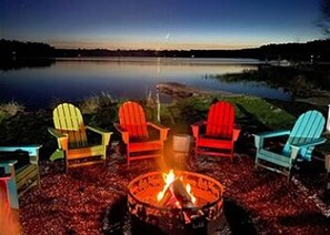 A lakeside setting with a fire pit and colorful Adirondack chairs.