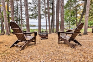 Twee Adirondack stoelen gericht op een meer, met een vuurkuil ertussen.