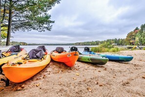 Kajaks rijden in een rij op een zanderig strand, met een meer en bomen op de achtergrond.