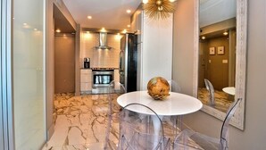 A modern kitchen with a central island, a dining area with a round table and clear chairs, and a large mirror on the wall. - OCEAN FRONT CONDO.  ENJOY YOUR MORNING COFFEE SITTING ON YOUR PRIVATE BALCONY WATCHING THE SUNRISE. (Rehoboth Beach)