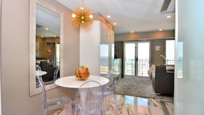 A modern hotel room with a round dining table, clear chairs, a large mirror, and a unique chandelier. - OCEAN FRONT CONDO.  ENJOY YOUR MORNING COFFEE SITTING ON YOUR PRIVATE BALCONY WATCHING THE SUNRISE. (Rehoboth Beach)