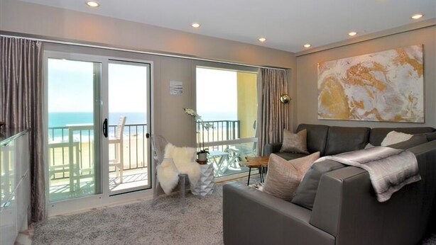 A spacious living room with a grey sofa, a white furry chair, and a large abstract painting on the wall. - OCEAN FRONT CONDO.  ENJOY YOUR MORNING COFFEE SITTING ON YOUR PRIVATE BALCONY WATCHING THE SUNRISE. (Rehoboth Beach)