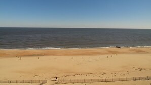 Una playa con cielo despejado, orilla arenosa y una persona caminando.