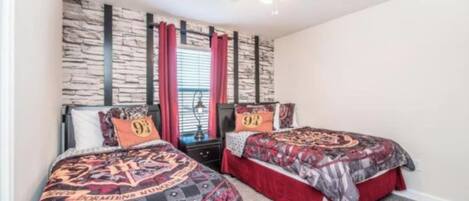 Un dormitorio con dos camas, pared con diseño de piedra, ventilador de techo y ventana con cortinas rojas.