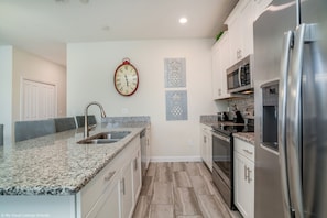 A modern kitchen with granite countertops, stainless steel appliances, and a clock on the wall. - Stunning Lakeview Townhome w/ Private Pool + Themed Bedrooms (Kissimmee)