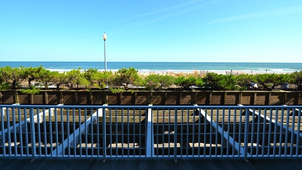Vista de una playa desde una terraza de madera con barandilla, con vista al océano y un cielo despejado.