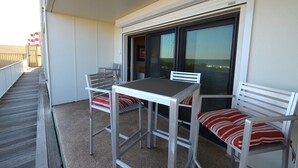 Un balcón con una mesa y dos sillas, un ventanal corredero y vista al mar.