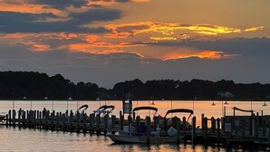 A waterfront dock with boats, a pier extending into calm water, and a backdrop of a sunset with clouds.