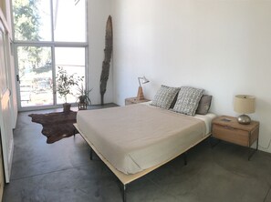 A bedroom with a large bed, a nightstand, a lamp, and a view of the outdoors through a window. - Modern design retreat in Downtown Durango (Durango)