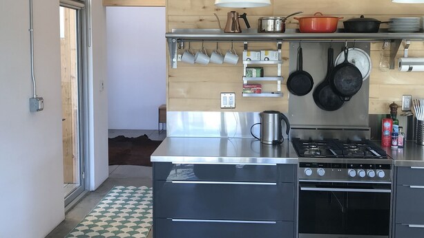 Una cucina moderna con elettrodomestici in acciaio inossidabile, pannelli murali in legno e pentole appese.