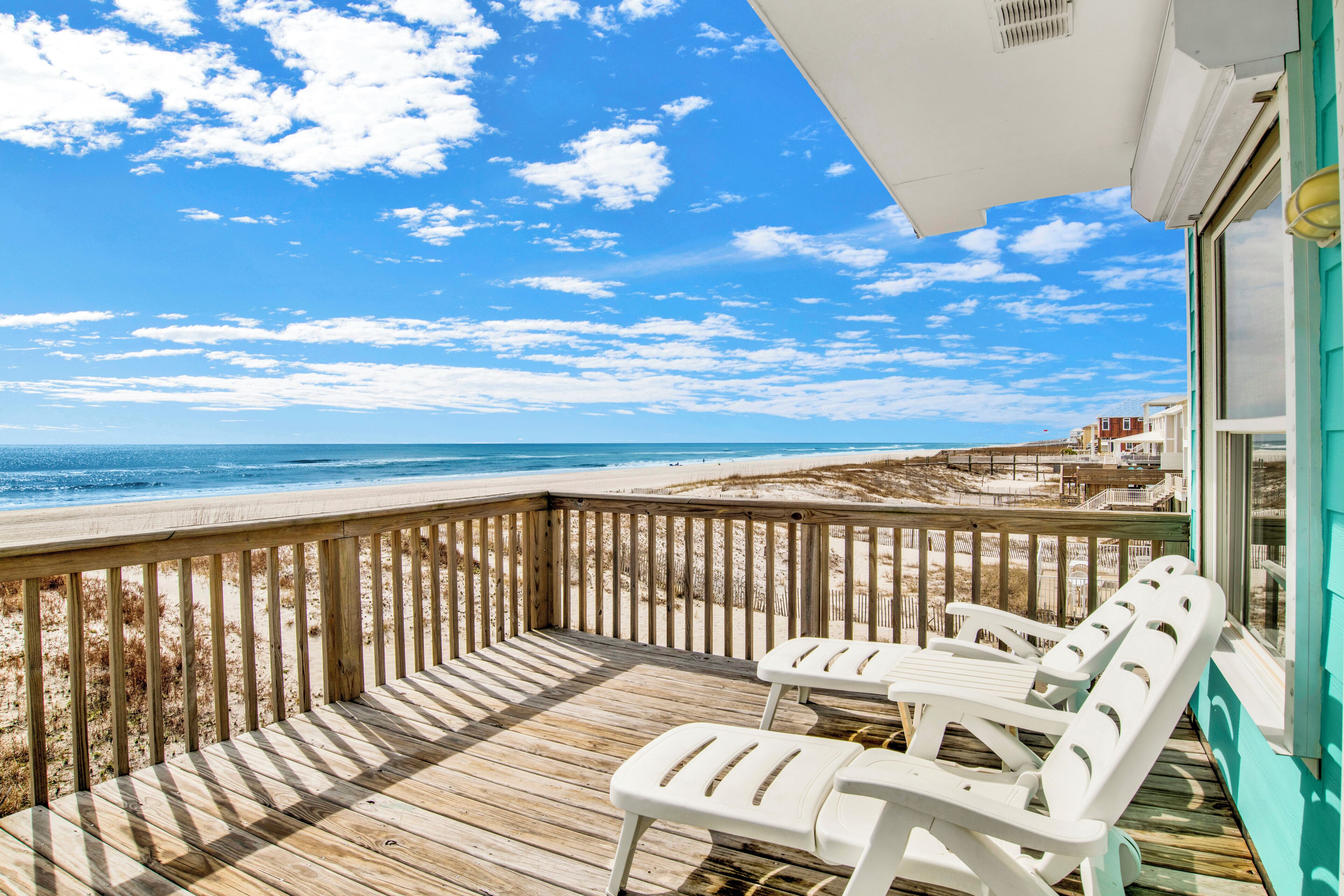 A wooden deck with white chairs overlooking a beach.
