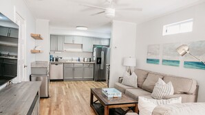 A modern kitchen with grey cabinets, a stainless steel refrigerator, and a dining area with a wooden table and beige sofa. - 65 Steps to Ocean • Private Home • 2-Car Garage (San Diego)