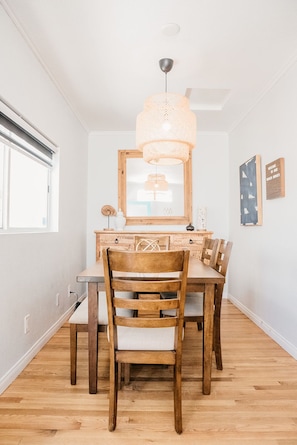 A dining area with a wooden table and chairs, a hanging light fixture, a framed mirror, and a wall-mounted sign. - 65 Steps to Ocean • Private Home • 2-Car Garage (San Diego)