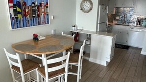 Una cocina moderna con armarios blancos, una mesa de comedor de madera con cuatro sillas, un reloj en la pared y un ventilador de techo.