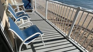 Un balcón con barandillas de metal blanco, una mesa y sillas azules con vista a la playa.