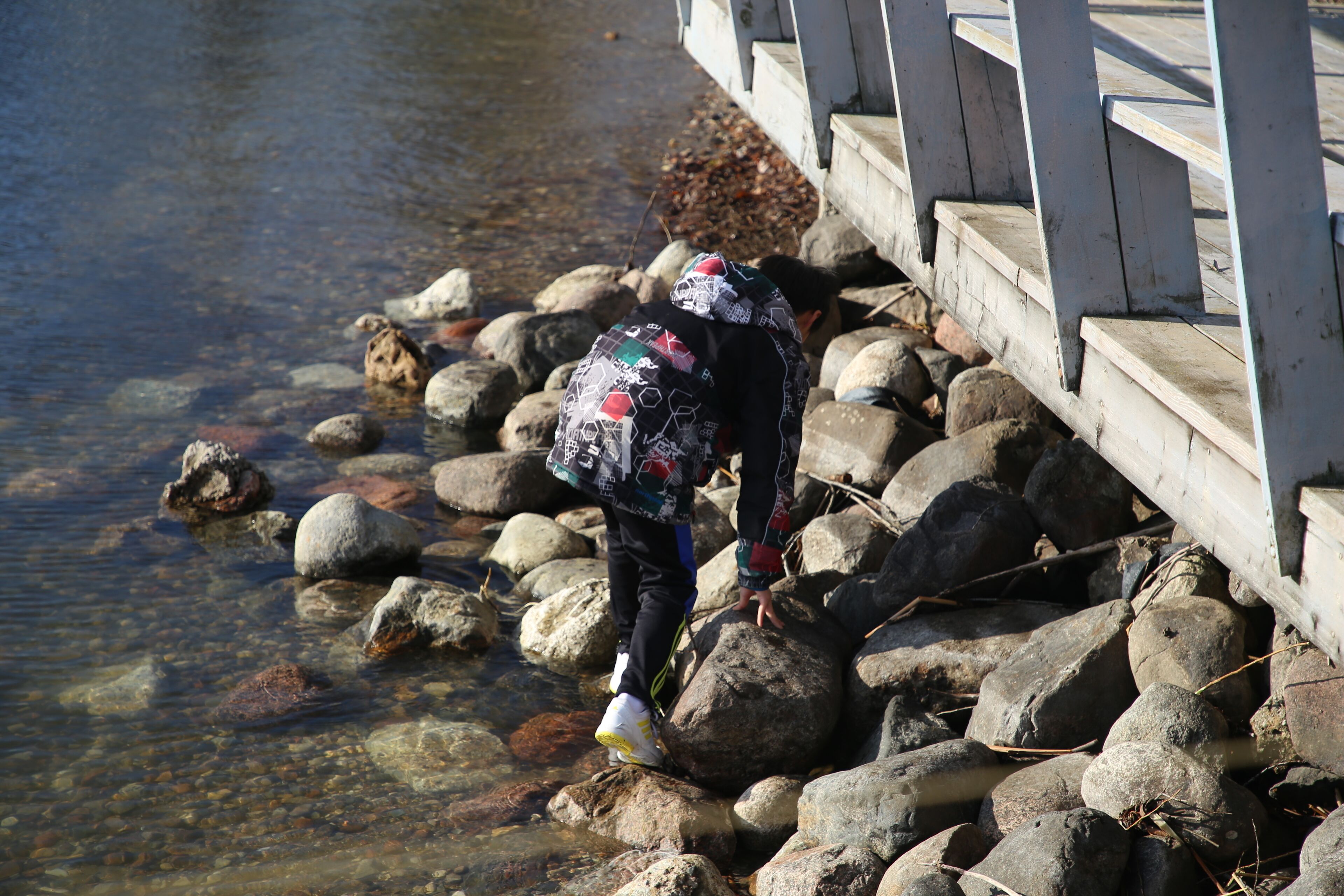 A person standing on rocks near a wooden bridge over a clear stream.