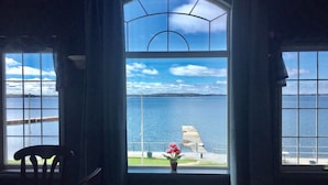 A room with a large arched window overlooking a body of water and a distant shoreline. - Home of 1000 Island#1-Directly on STL  river, private beach & FREE boat docking  (Gananoque)