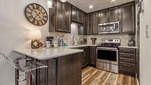 Una cocina moderna con armarios de madera oscura, electrodomésticos de acero inoxidable, un reloj grande y una barra con taburetes.