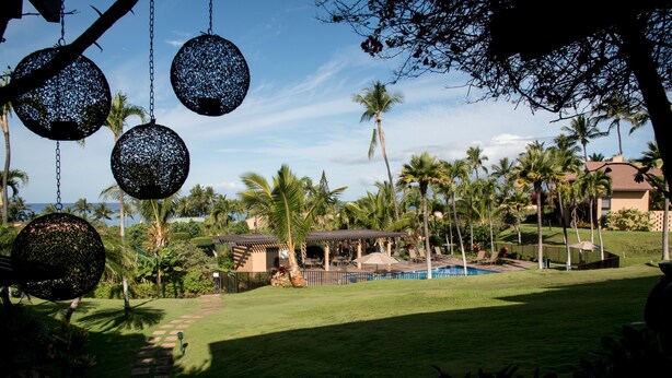 A resort with a swimming pool, palm trees, and hanging decorative spheres. - Ekahi 29C, Ocean View,  Steps away from the pool (Wailea)