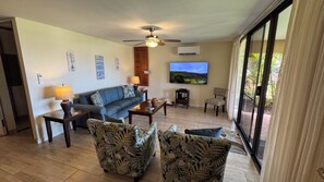 A living room with a sofa, two armchairs, a coffee table, a TV, and a ceiling fan.