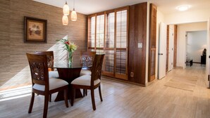 A dining area with a wooden table and chairs, a vase with flowers, and a large window with wooden shutters. - Ekahi 29C, Ocean View,  Steps away from the pool (Wailea)